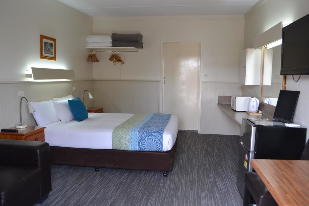 A hotel room with a bed, bedside table, lamp, TV, and a desk with a chair.