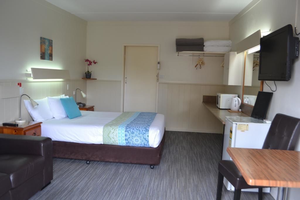 Ein Hotelzimmer mit einem Bett, einem Schreibtisch mit Computer, einem Sessel, einem Fernseher und einer Mikrowelle.