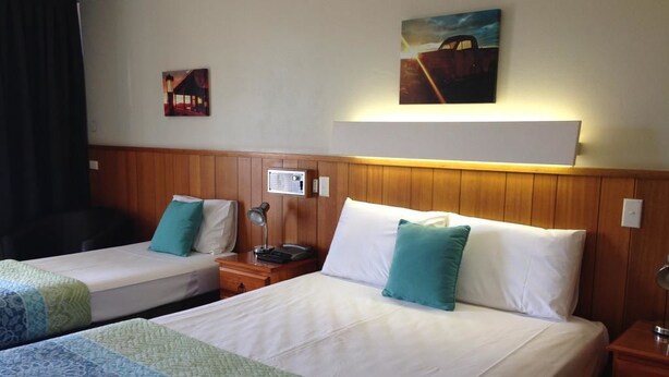 A hotel room with two single beds, a wooden headboard, a nightstand with a lamp, and a painting on the wall.