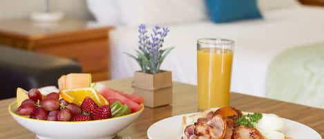 A breakfast table with a bowl of fruit, a plate of eggs and bacon, and a glass of orange juice.