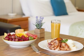 A breakfast table with a bowl of fruit, a plate of eggs and bacon, and a glass of orange juice. - Gatton Motel (Gatton)