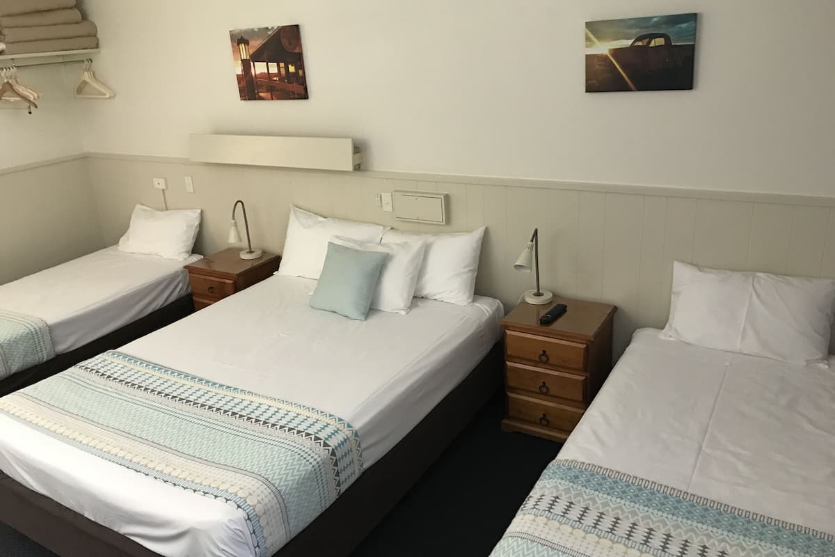 Quarto de hotel com duas camas de solteiro, mesa de cabeceira com abajur e prateleira na parede.