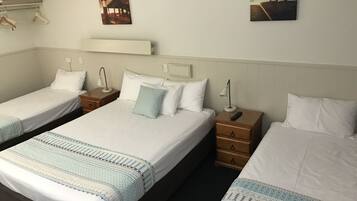 A hotel room with two single beds, a nightstand with a lamp, and a wall-mounted shelf.