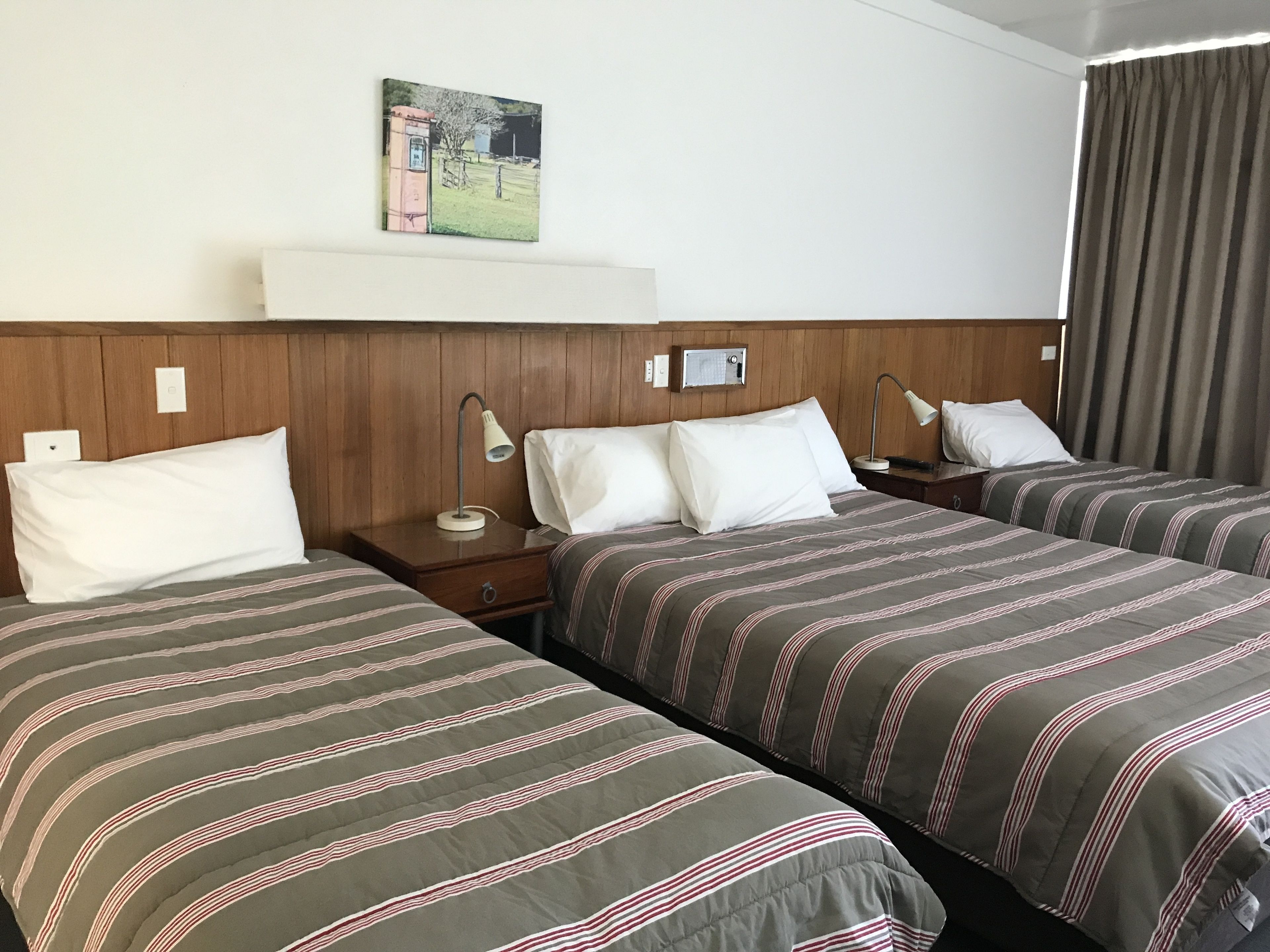 A hotel room with two single beds, wooden headboards, bedside lamps, a small table, and a painting on the wall.