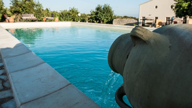A swimming pool with clear blue water, a stone border, and a large stone structure in the foreground.