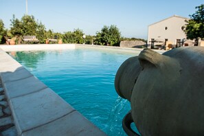 A swimming pool with clear blue water, a stone border, and a large stone structure in the foreground. - farmhouse I 5 SENSI (Modica)