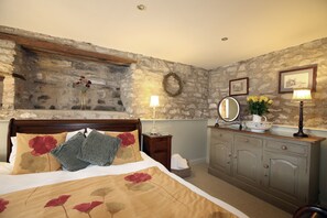 A bedroom with a stone wall, a wooden bed, a dresser, and a mirror. - Converted stable Mews Cottage with one king bed Sleigh bedroom (Kirkbymoorside)