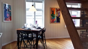 Et spiseområde med et træbord dækket til fire personer, omgivet af sorte stole. En hængende lampe er placeret over bordet.