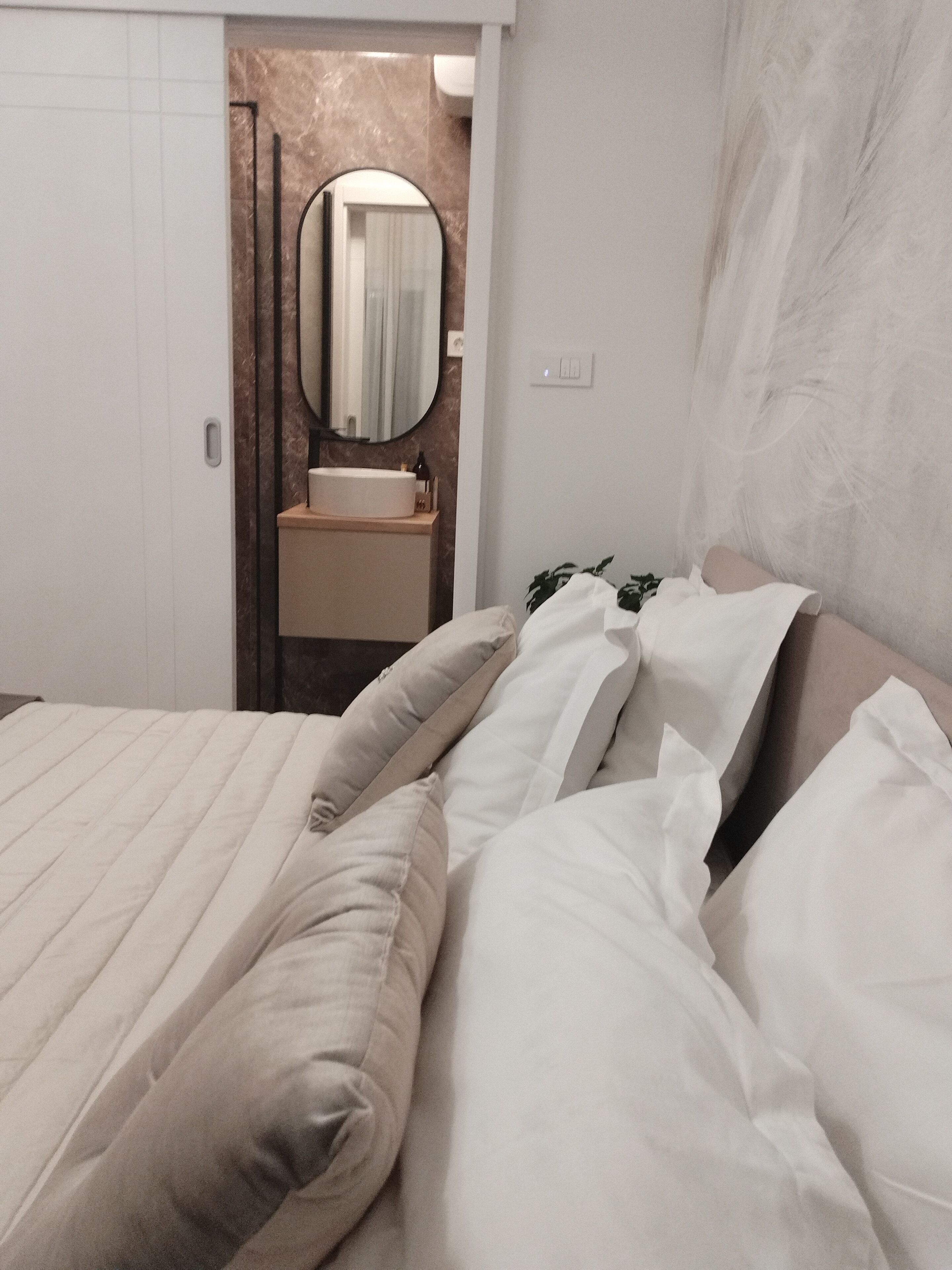 Een hotelkamer met een bed, een badkamer met een wastafel en spiegel, en een deur die naar een andere kamer leidt.