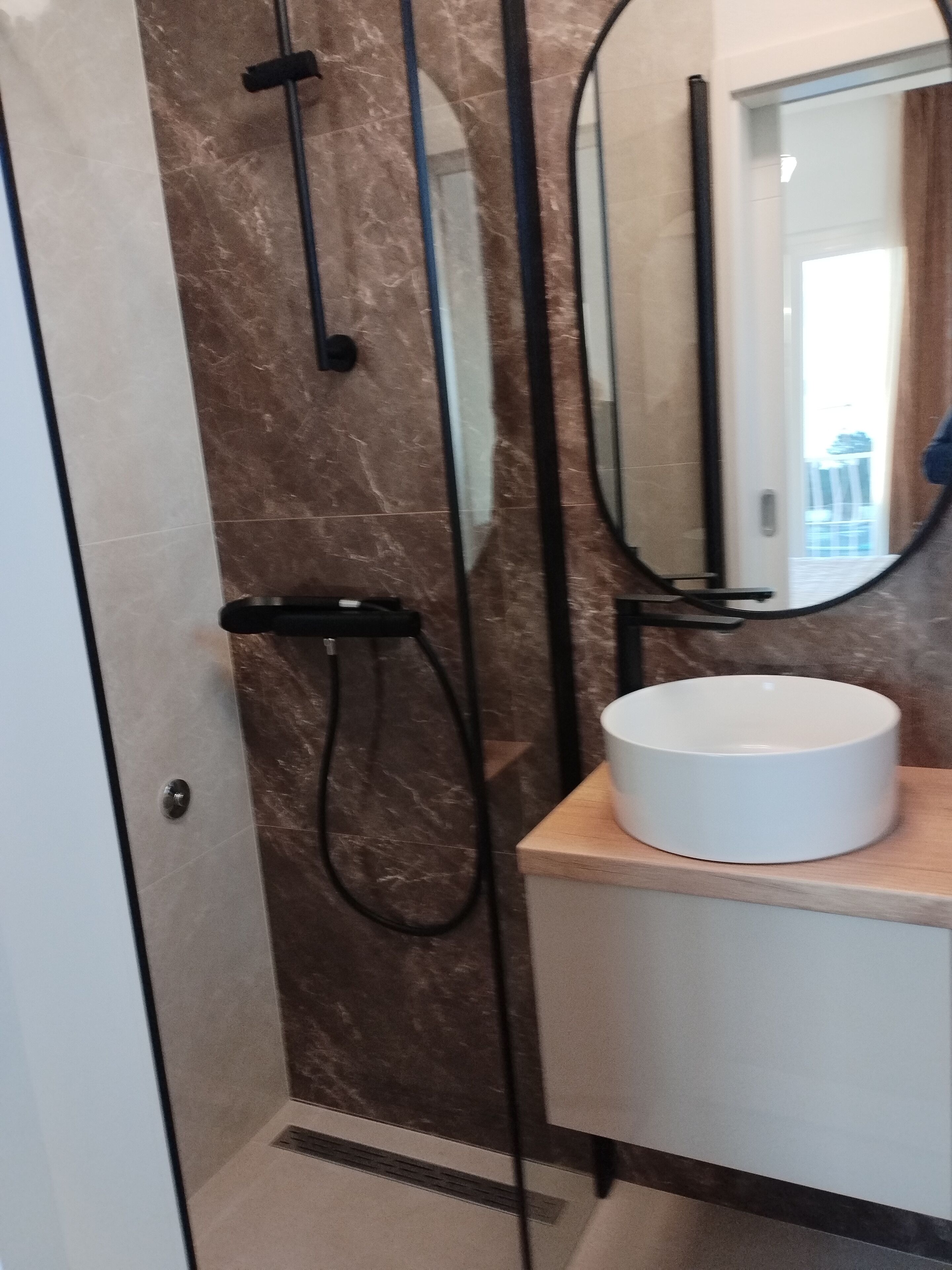 Een moderne badkamer met een douchecabine van glas, een wit wastafeltje en een spiegel erboven.