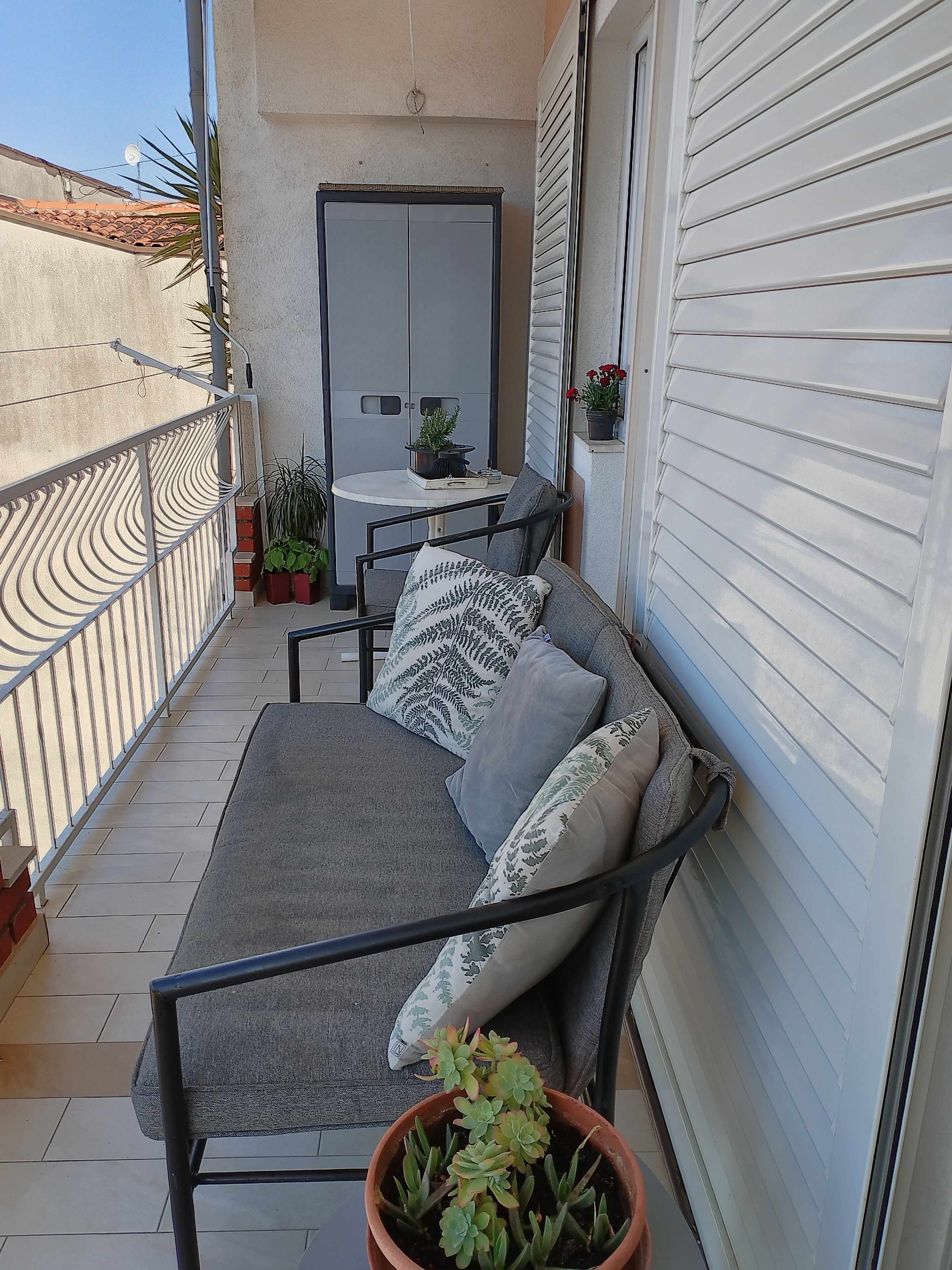 Un balcon avec un canapé gris, une petite table et des plantes en pot.