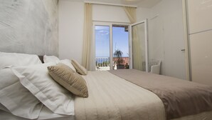 Ein Schlafzimmer mit einem großen Bett, Blick auf einen Balkon und einer modernen Pendelleuchte.