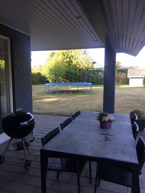 An outdoor patio with a table and chairs, a barbecue grill, and a trampoline in the background.