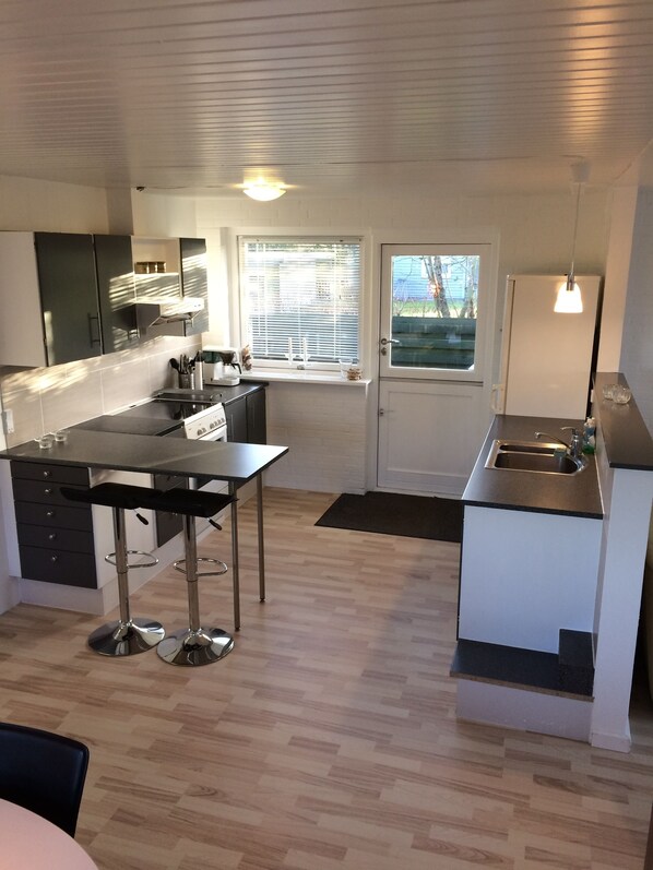 A modern kitchen with a black countertop, stainless steel appliances, and a window with blinds.