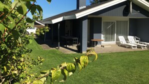Ein modernes Haus mit überdachter Terrasse, Rasenfläche und einem geparkten Auto in der Nähe.