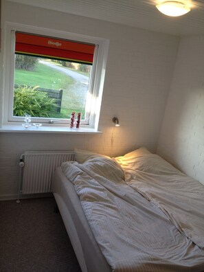 A small, single-bed room with a window, a radiator, and a bedside table.