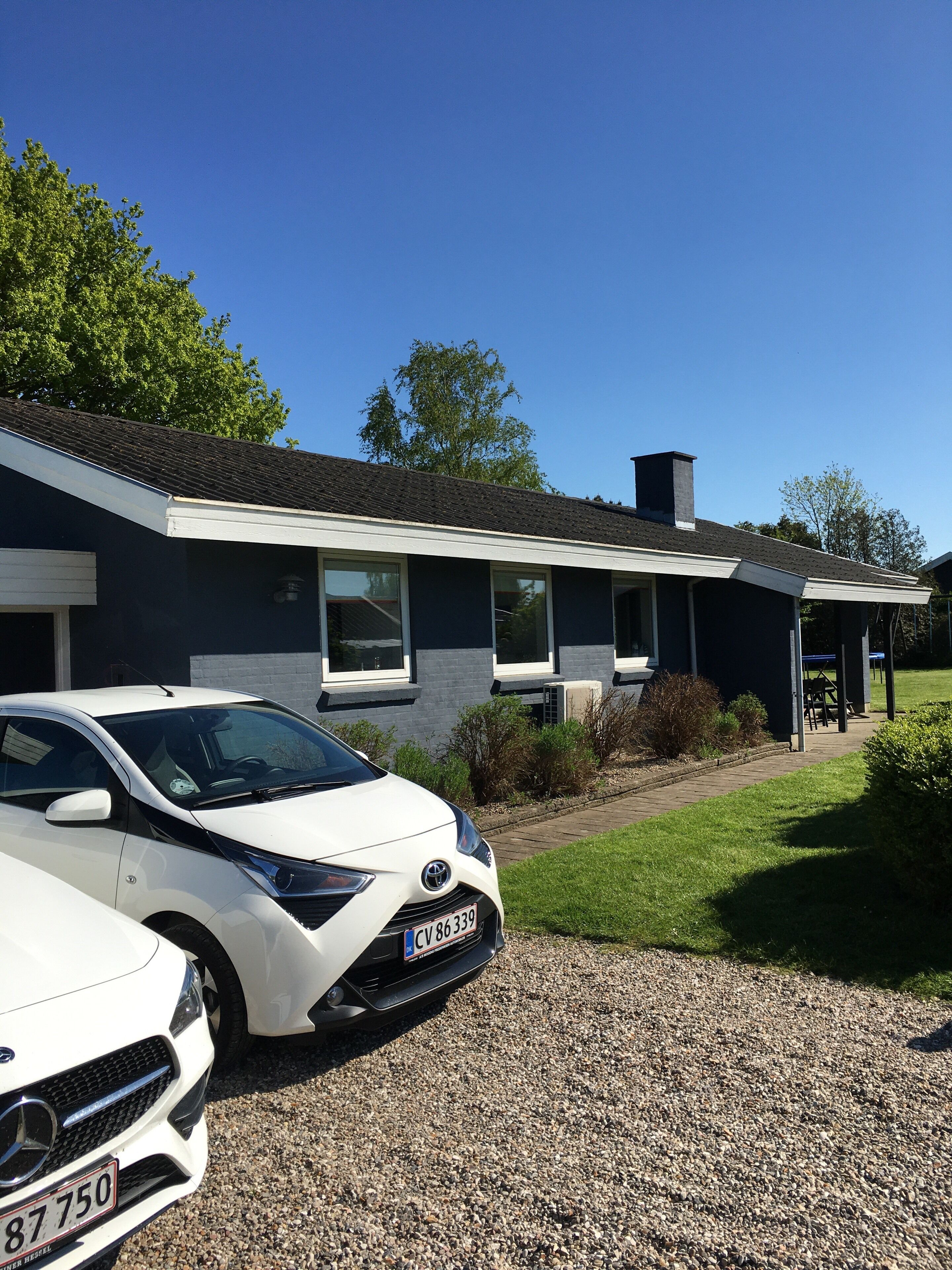 Een modern huis met twee verdiepingen, met een grindpad en een witte auto ervoor geparkeerd.