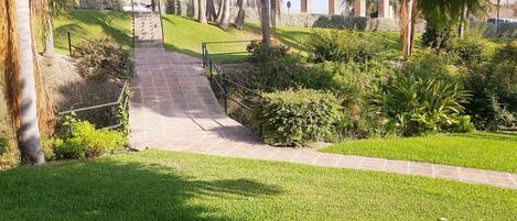 A pathway leading to a bridge with arches, surrounded by well-maintained grass and palm trees.