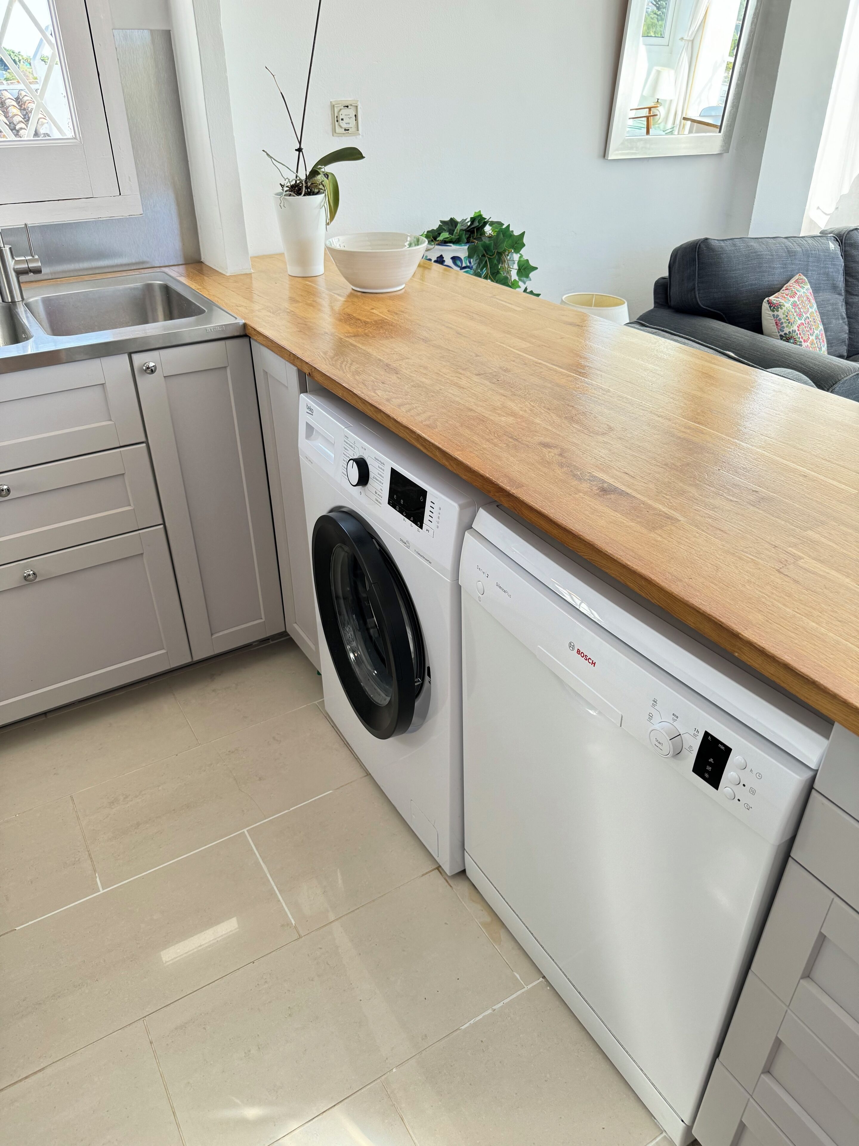 Une cuisine compacte équipée d’un lave-linge, d’un évier et d’un plan de travail en bois.