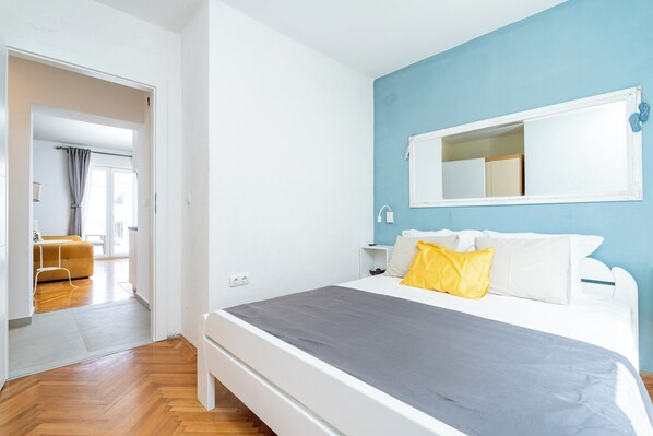 A bedroom with a bed, a nightstand, a mirror, and a window.