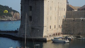 A historic stone tower with a flag, a harbor with boats, and a coastal landscape. - 2 bedroom, 2 bathroom Apartment in Lapad with a large terrace and parking (Dubrovnik)