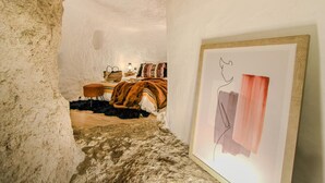 A room with a bed, a chair, a table, and a framed artwork on the wall. - HOHLE Cave Suite (Cave Hotel Lomas de Ruvira) (Jorquera)