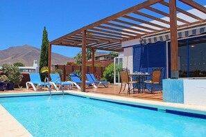 A pool area with blue lounge chairs, a wooden pergola, and a table with chairs. - Lovely Villa, Air-con,Free Wi-Fi & Private Pool, In Las Coloradas,Playa Blanca. (Playa Blanca)
