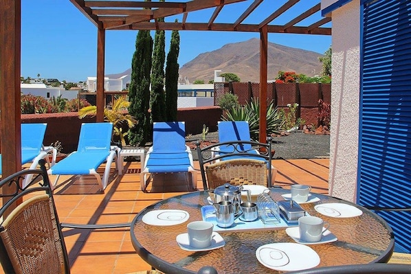 A patio with blue lounge chairs, a round table set for four, and a mountain view in the background.