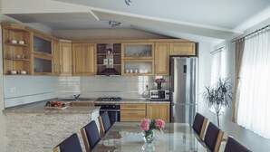 A modern kitchen with wooden cabinets, a central island, and a dining area with a glass table and chairs. - COZY HOUSE HEATED POOL, NEAR BEACH IN SPLIT COUNTY (Imotski)