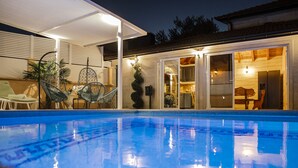 A swimming pool with a clear blue surface, surrounded by a covered patio area with chairs and a dining table. - COZY HOUSE HEATED POOL, NEAR BEACH IN SPLIT COUNTY (Imotski)