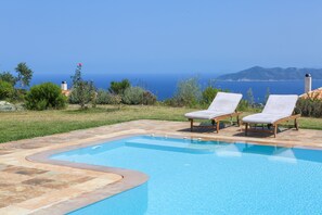 A swimming pool with two lounge chairs, surrounded by a stone patio, with a view of the sea and distant mountains. - ANGIO LUXURIUS VILLAS IN SKIATHOS (SKIATHOS)