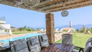 A poolside area with lounge chairs, a wooden table, and a view of the sea. - ANGIO LUXURIUS VILLAS IN SKIATHOS (SKIATHOS)