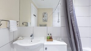 Un baño moderno con lavamanos, tocador y ducha blancos.