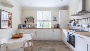 Una cocina moderna con armarios blancos, encimera de madera, estufa a gas y una ventana con persianas.