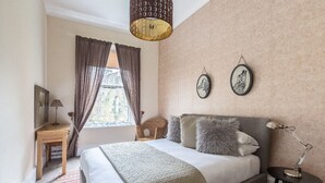 Un dormitorio con cama, mesita de noche, lámpara, ventana con cortinas y decoración en la pared.