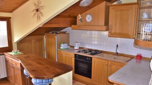 Een keuken met houten kastjes, een fornuis, een spoelbak en een klok aan de muur.