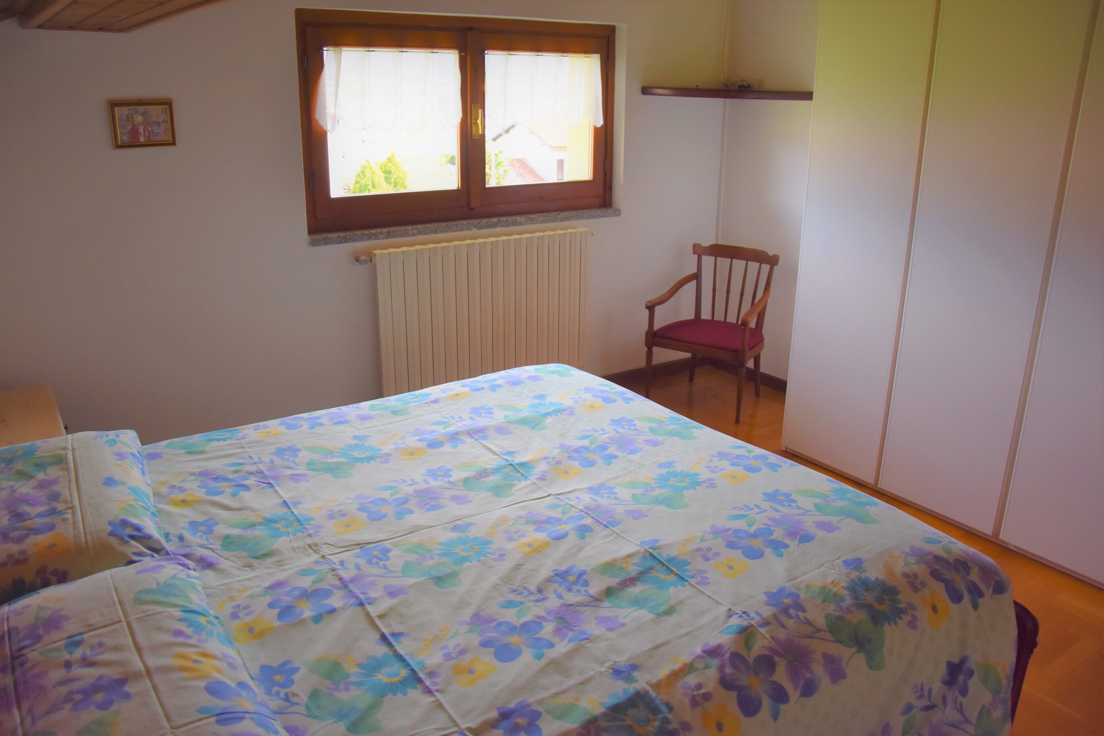 A bedroom with a bed, a chair, a window, and a radiator.