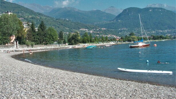 Een kiezelstrand met boten, een heldere lucht en bergen op de achtergrond.