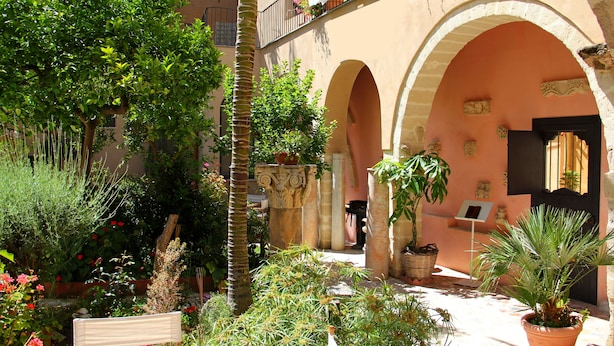 Un patio con arcos, plantas en macetas y un banco.