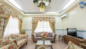 A living room with floral-patterned sofas, a glass coffee table, a television, and a decorative ceiling light. -  Family villa with pool on Panglao Island close to beach and dive sites (Panglao)