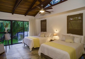 Habitación de hotel con dos camas, ventilador de techo y vistas al exterior.
