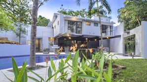 Een modern huis met twee verdiepingen, een zwembad, omringd door tropische planten en palmbomen.