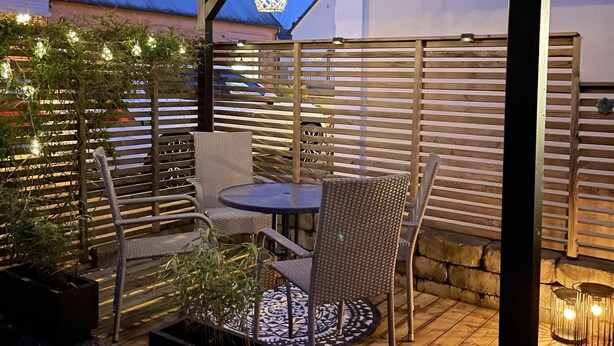Een houten terras met een pergola, tuinmeubilair en lichtjes.