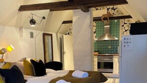 Een slaapkamer met een bed, kussens, een bedlampje, een houten plafond en een keuken met een koelkast.