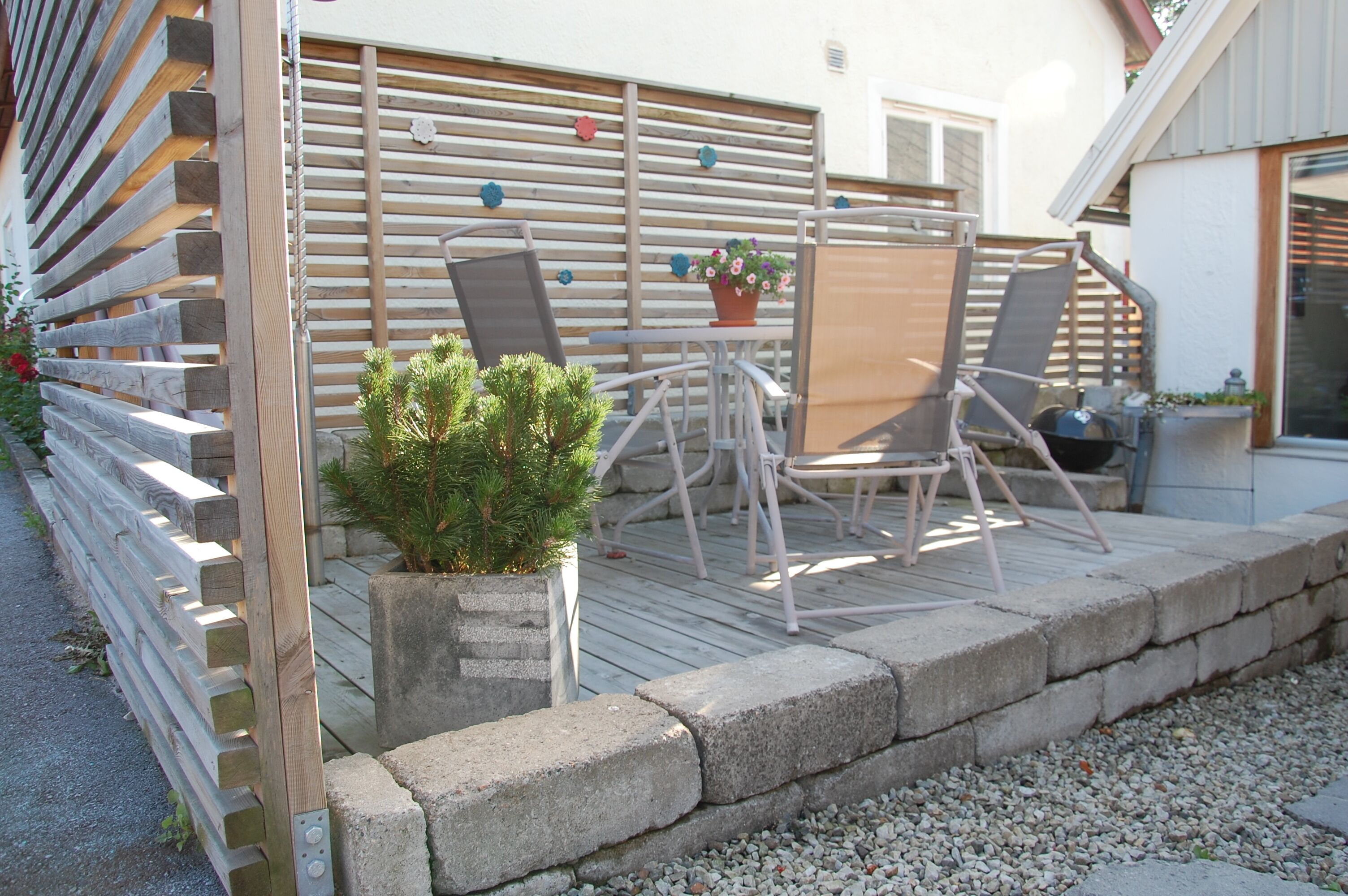 A patio with a wooden fence, a small table with chairs, and a potted plant.