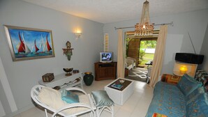 A living room with a sofa, a wicker chair, a television, and a painting on the wall.