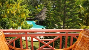 A tropical resort with a pool, lush greenery, and a thatched-roof hut.