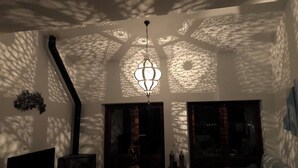 Une pièce dotée d’un plafond au design original qui projette des ombres, d’un luminaire suspendu et d’un lit recouvert d’une couverture blanche.