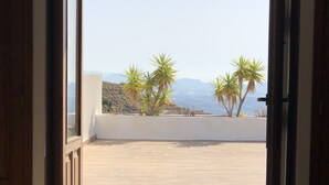 Une porte ouverte donnant sur une terrasse d’où l’on peut admirer des palmiers et des montagnes au loin.