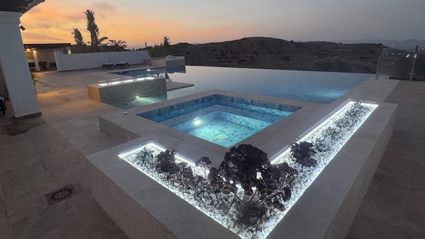 Une piscine à débordement offrant une vue sur le paysage, un espace salon et une zone bien éclairée au bord de la piscine.